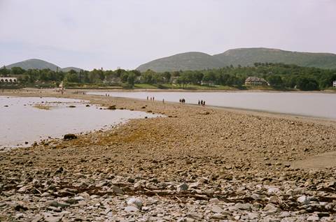 People walking across an exposed sand bar between an island and the mainland