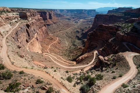 A light beige unpaved road winds back and forth down colorful sandstone walls.