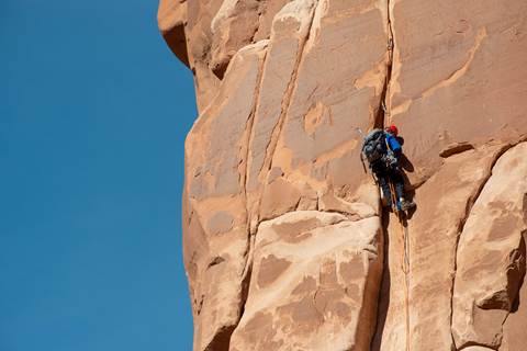 rock climber on vertical tan sandstone face, blue sky in background