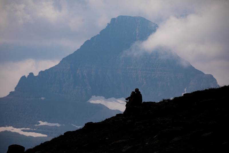people sitting on a hill with clouds and mountain behind