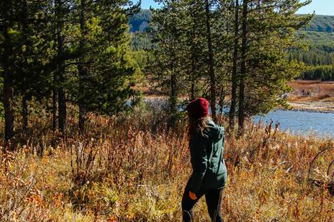 A female hiker walks along a wooded trail by a river.