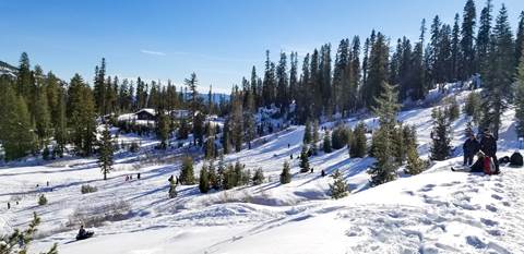 A landscape photo of a snow-covered hill with people playing and a building in the background.