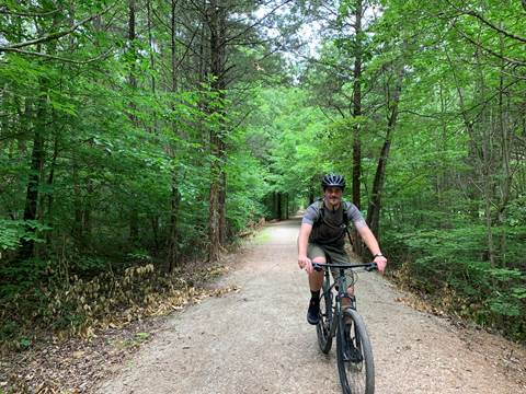 A young man rides a bike alone on a gravel trail.