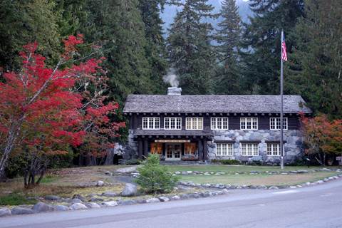 A wood and stone historic building framed by conifer trees and vine maples with red foliage.