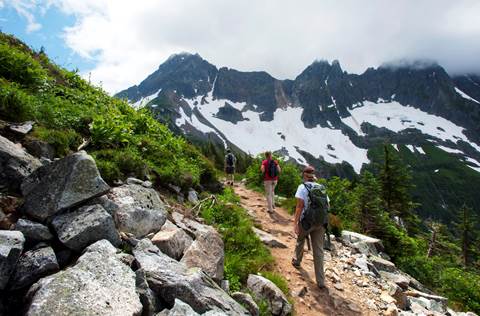 Two hikers walk along a trail with mountains in the distance.