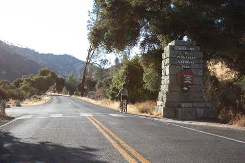 Visitor seen along a paved roadway riding a bicycle past a park service sign made into a rock pillar